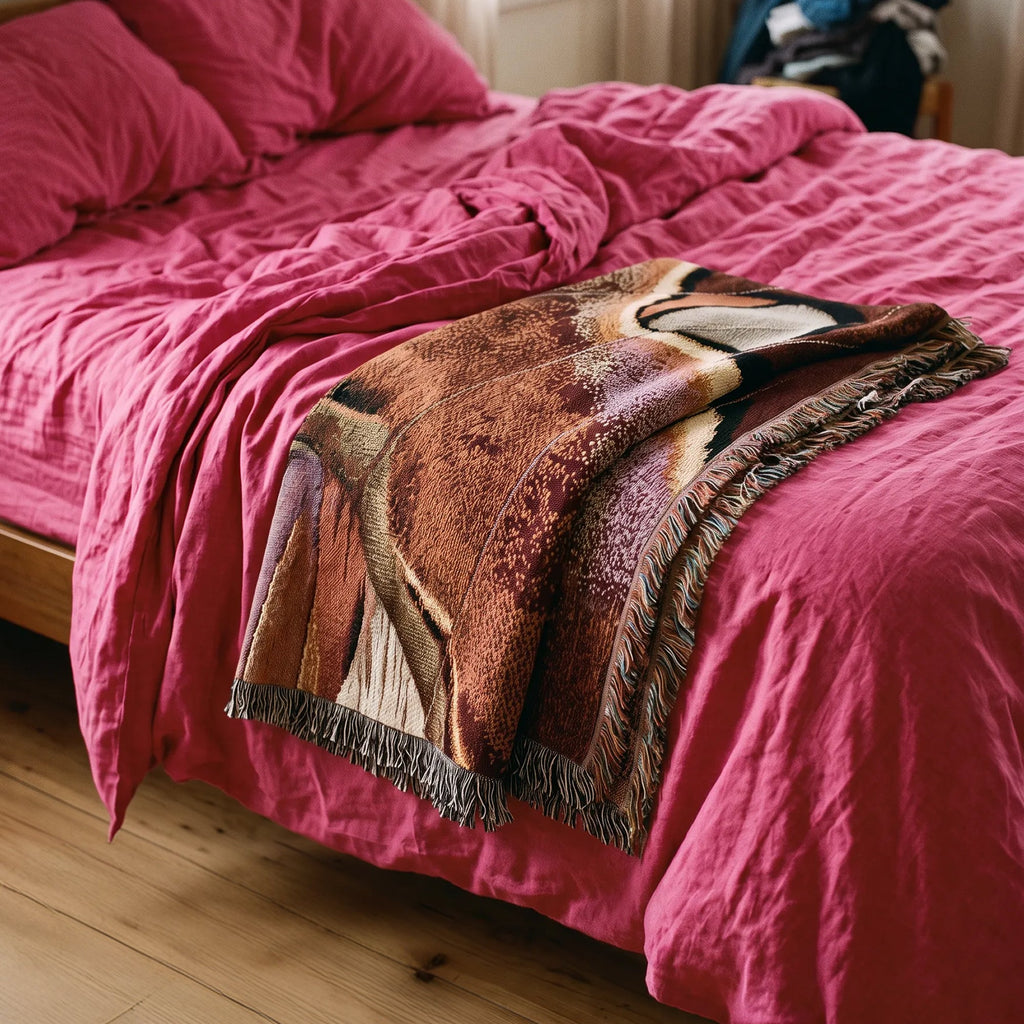 A close-up of a bed with bright pink bedding and a folded throw blanket featuring a brown, beige, and black animal print with fringe.